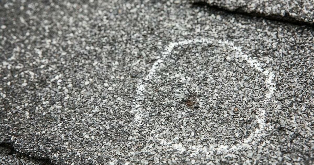 Close-up of hail-damaged roof shingles showing circular impact marks and granule loss
